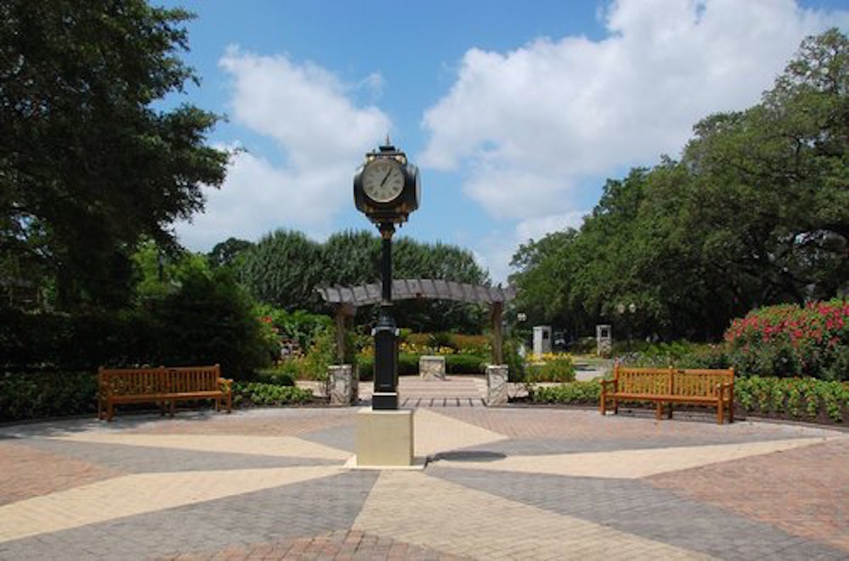 A park scene featuring a vintage clock and benches under a partly cloudy sky.